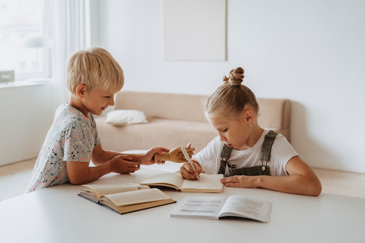 Blonde boy and girl studying together indoors, focusing on writing and learning.